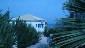 A coastal building with a tiled roof, surrounded by lush greenery and a clear view of the sea. - Βίλα Μιχάλης  πανόραμα (Kombi)