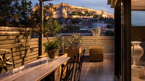 A terrace with a table and chairs, potted plants, and a view of a historic hilltop. - Fos Residential Apartments (Athens)