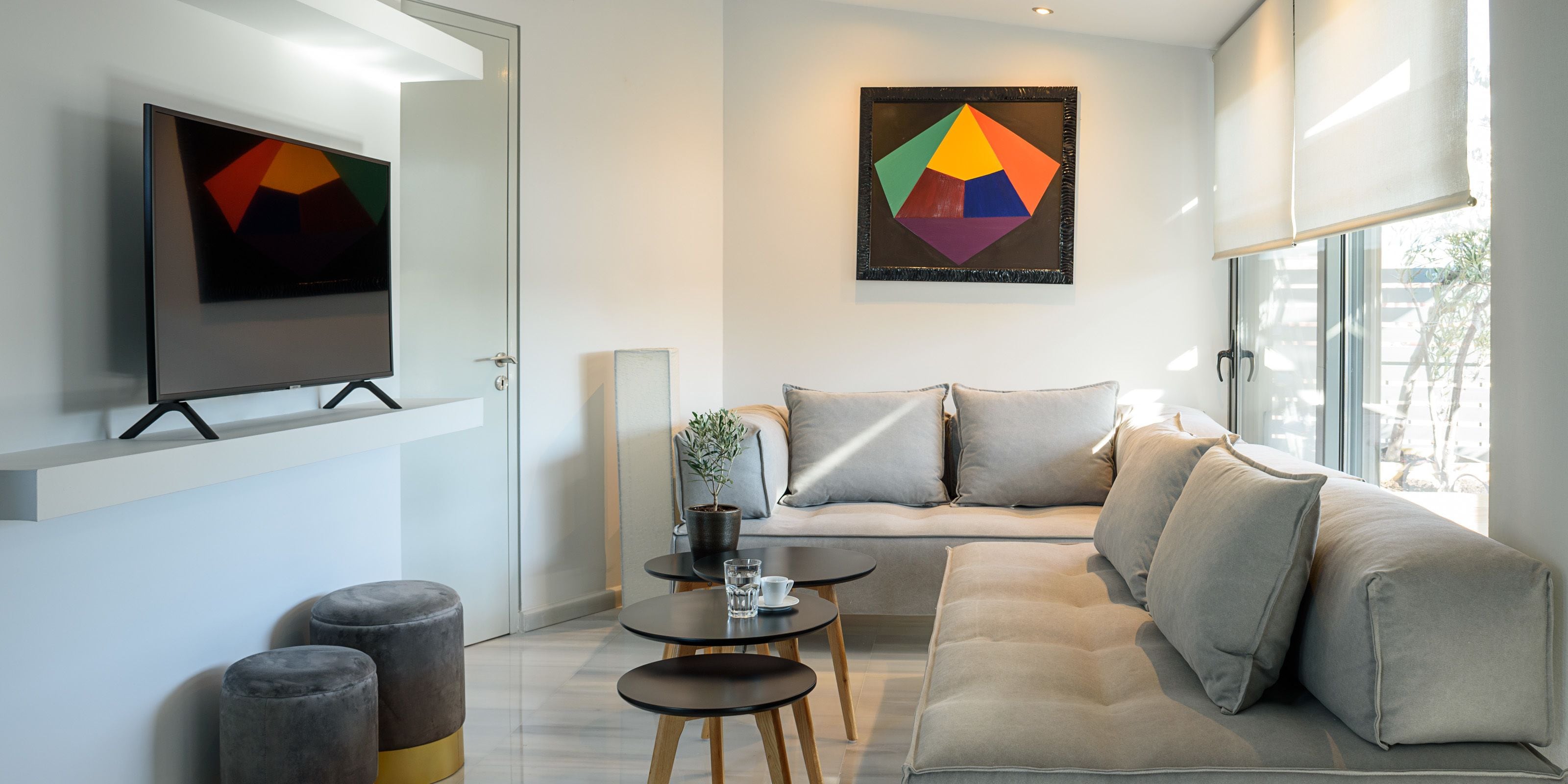 Un salon moderne avec un canapé, deux petites tables et un téléviseur posé sur un meuble.