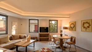 A modern living room with a sofa, coffee table, TV, and dining area. - Fos Residential Apartments (Athens)