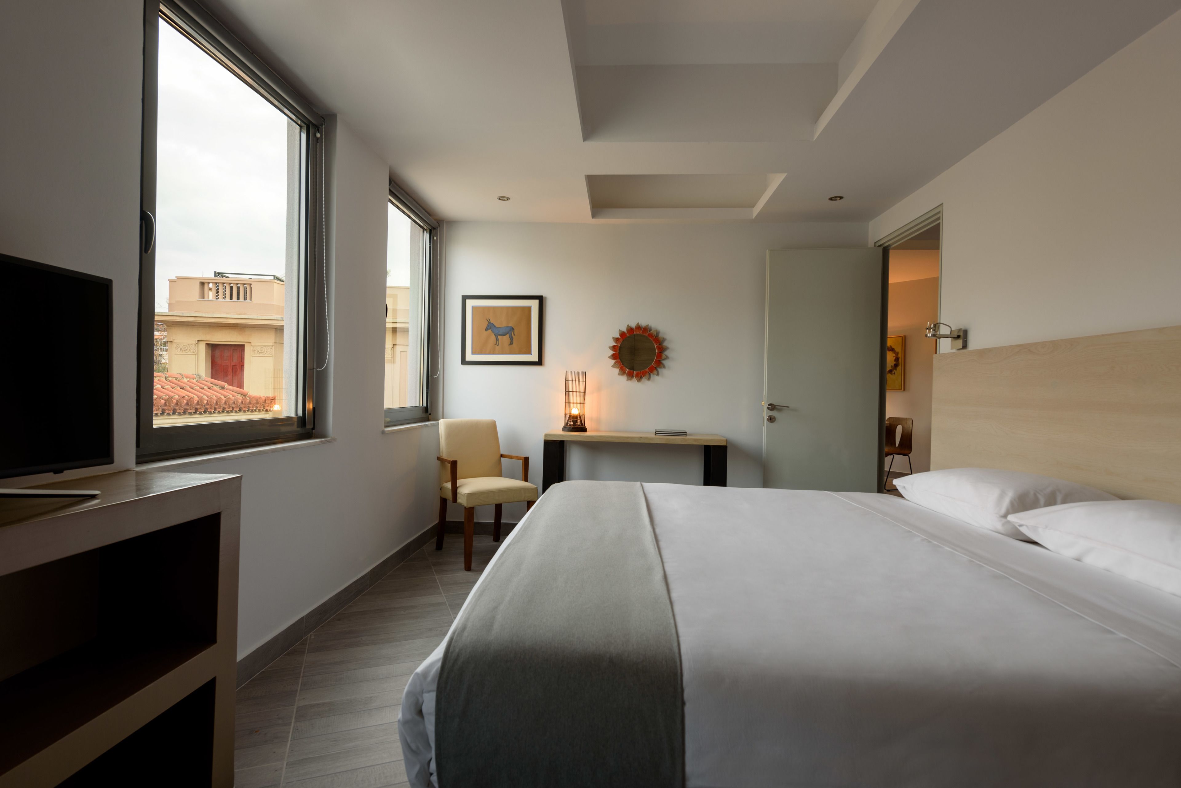 A hotel room with a bed, a desk, a chair, a television, and a window with a view of buildings.