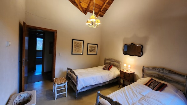Un dormitorio con dos camas, techo de madera, candelabro, cuadros enmarcados y una pequeña mesa con lámparas.