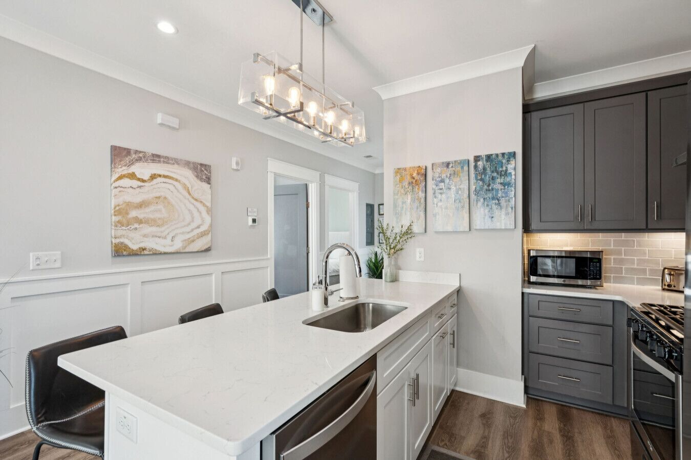 A modern kitchen with a large island, gray cabinets, and a stainless steel range hood.
