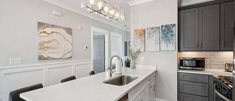 A modern kitchen with a large island, gray cabinets, and a stainless steel range hood.
