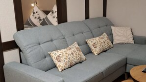 A light grey sectional sofa with floral patterned cushions, a round wooden coffee table, and a wall-mounted light fixture. - Zum Weingutsmuseum (Cochem)