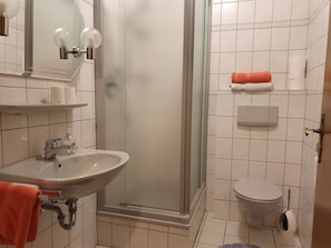A bathroom with a sink, mirror, glass shower enclosure, toilet, and a towel rack. - Zum Weingutsmuseum (Cochem)