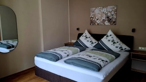 A neatly made bed with floral pillows, a bedside table, a wall-mounted mirror, and a painting above the bed. - Zum Weingutsmuseum (Cochem)