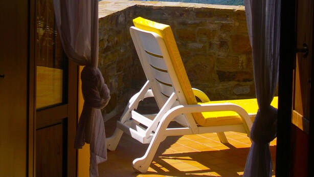 A room with a view of the sea, a white chair, and curtains.