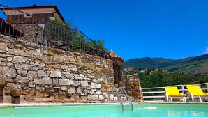 A stone building with a pool and yellow lounge chairs.