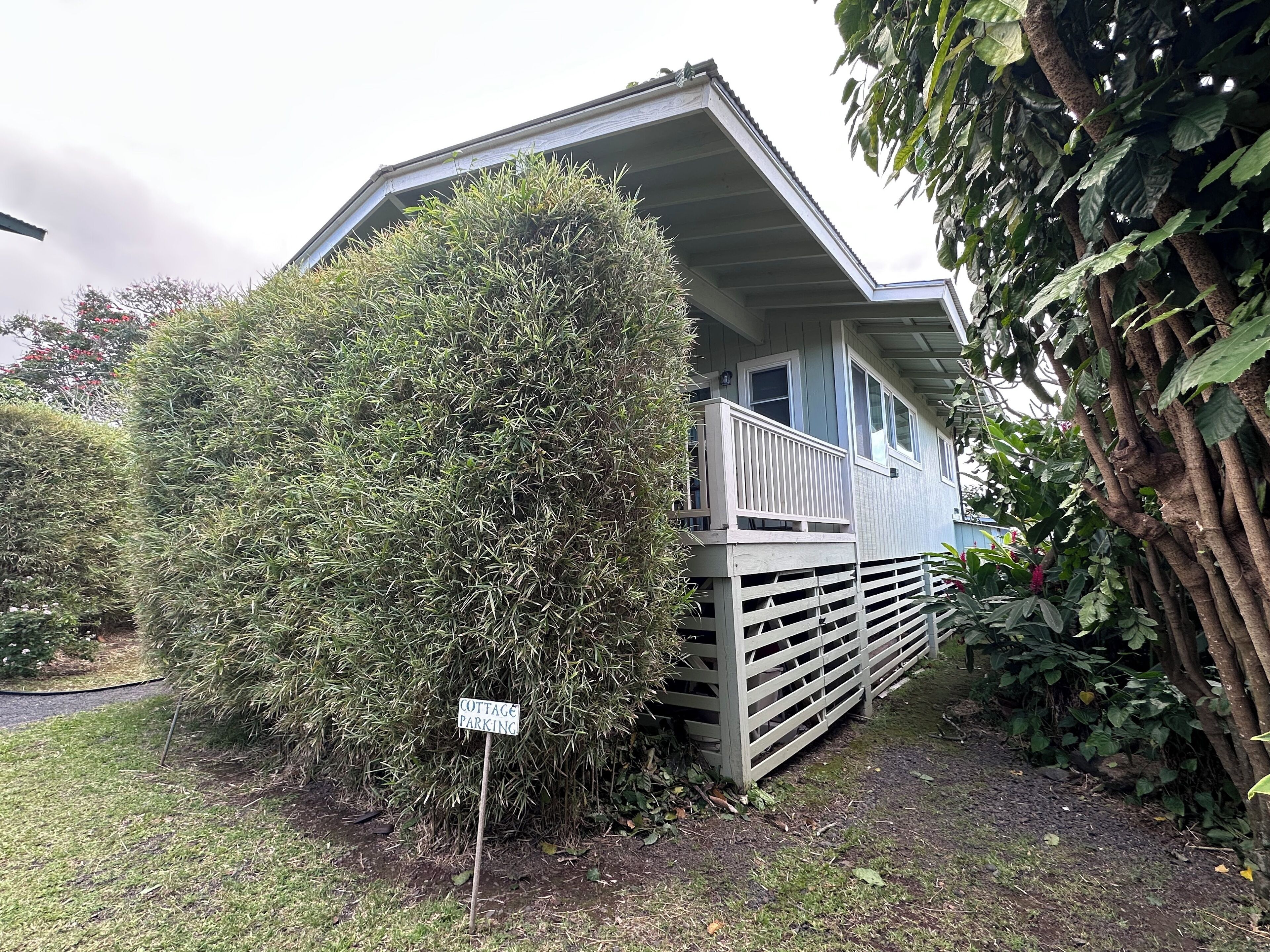 Ein Cottage mit einer überdachten Veranda, umgeben von dichtem Grün und einem Schild mit der Aufschrift 'COTTAGE PARKING'.