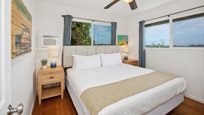 Ein Schlafzimmer mit einem Bett, zwei Nachttischen, einem Deckenventilator und großen Fenstern.