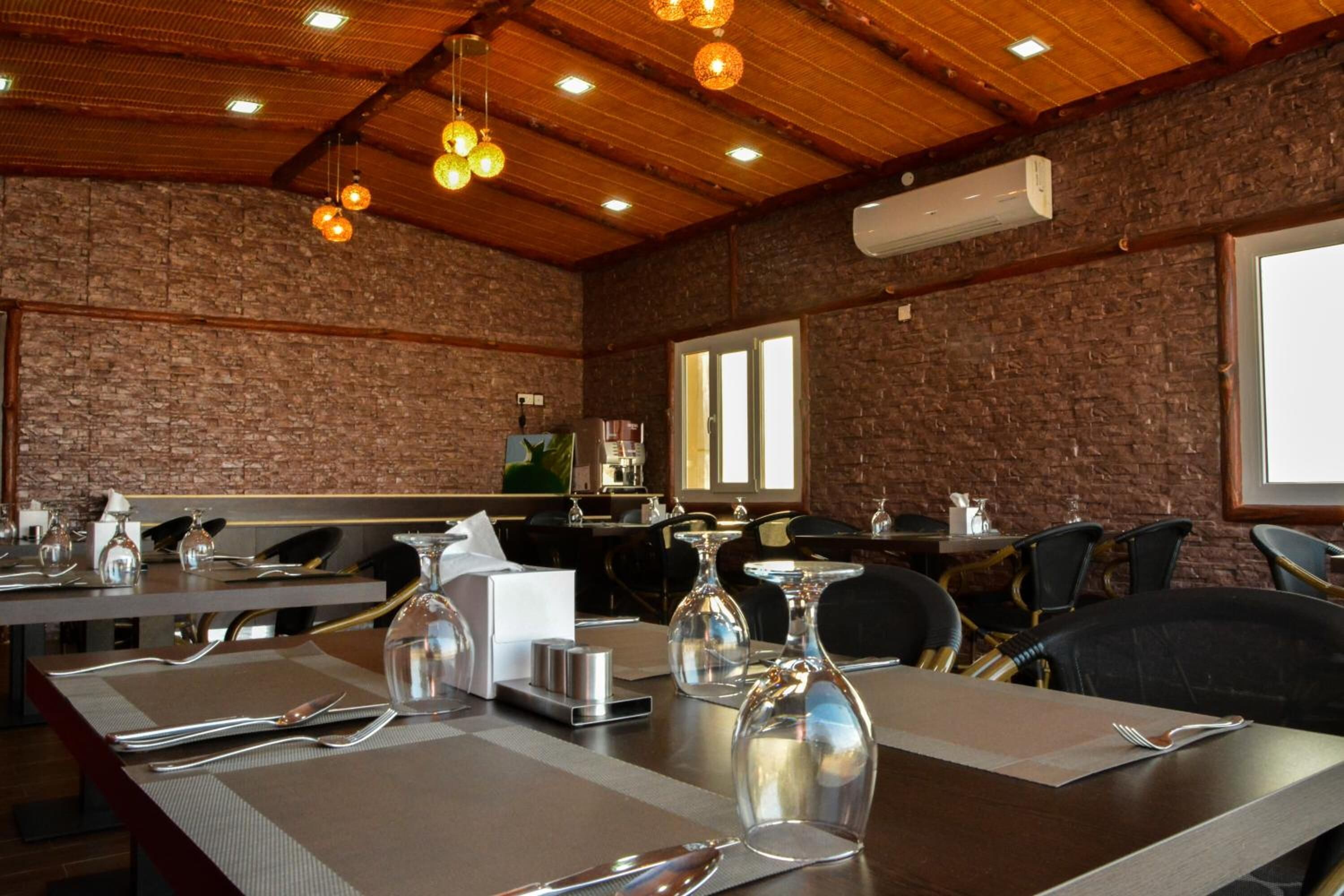 A restaurant with brick walls, wooden ceiling, and hanging light fixtures. Tables are set with cutlery and glassware.