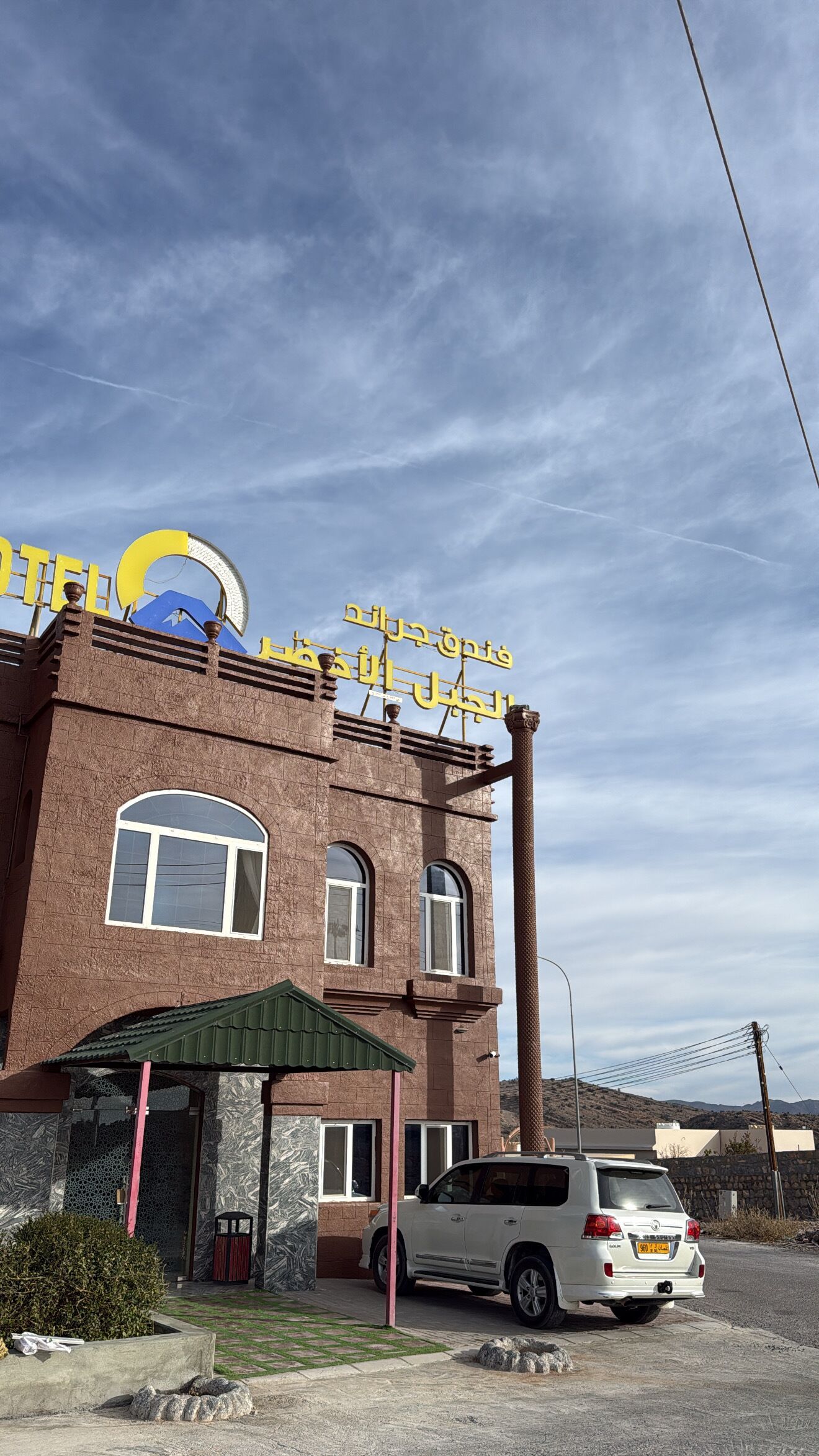 Un hotel con un letrero llamativo, fachada de ladrillo y un coche estacionado.
