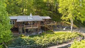 A two-story wooden cabin with a stone foundation, a covered deck, and a stone wall. - 'View & Far Between' Cozy Mountain Home w/ hot tub (Ashe County)