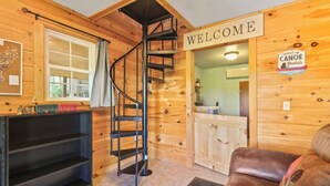 A wooden interior with a spiral staircase, a welcome sign, a paddle on canoe rentals sign, and a brown leather couch. - 'View & Far Between' Cozy Mountain Home w/ hot tub (Ashe County)