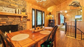 A wooden interior with a stone wall, a fireplace, a dining table with chairs, and a staircase. - 'View & Far Between' Cozy Mountain Home w/ hot tub (Ashe County)