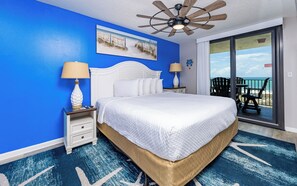 A hotel room with a bed, two nightstands, a ceiling fan, a painting, and a view of the beach. - Panoramic Views! - Phoenix VII 7513 (Orange Beach)