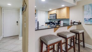 A kitchen with wooden cabinets, a black countertop, and a microwave. There are three bar stools with cushioned seats. - Beach Days = Best Days!   Fishing, Sunning, Beaching, Boating, Swimming=FUN!! (Biloxi)