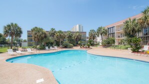 A swimming pool with lounge chairs, palm trees, and a building with balconies in the background. - Beach Days = Best Days!   Fishing, Sunning, Beaching, Boating, Swimming=FUN!! (Biloxi)