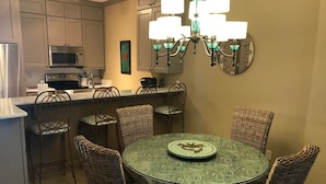A kitchen with a dining area, featuring a round table with chairs, a chandelier, and a clock on the wall.
