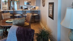 A modern kitchen with a central island, dining area with wicker chairs, and a chandelier.