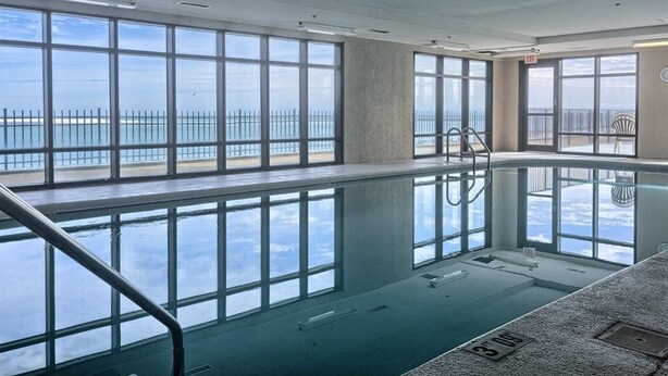 An indoor swimming pool with large windows offering a view of the sea.