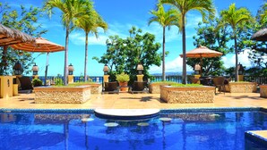 A pool area with lounge chairs, umbrellas, and palm trees.