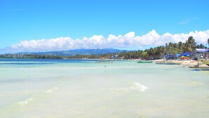 A beach with clear turquoise water, boats, and palm trees.