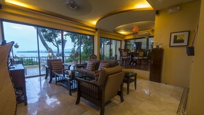 A spacious living area with a large window overlooking the sea, furnished with a sofa, chairs, and a coffee table.