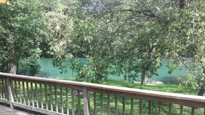 A wooden deck with a railing overlooking a green lawn and trees.