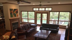 A spacious living room with a fireplace, leather sofas, a coffee table, and large windows offering a view of the outdoors.