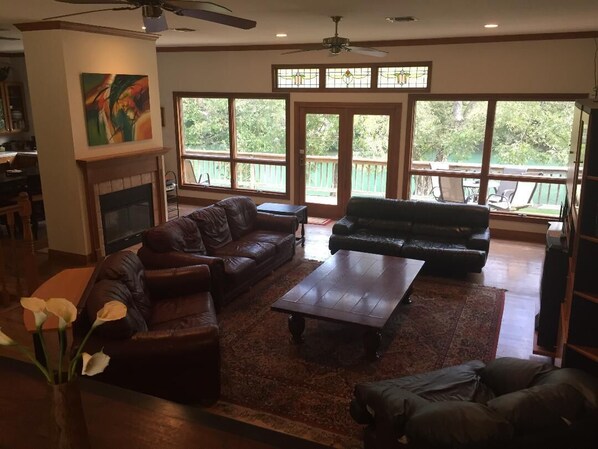A spacious living room with a fireplace, leather sofas, a coffee table, and large windows offering a view of the outdoors.