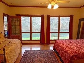 Un dormitorio con dos camas, un ventanal con cortinas, un ventilador de techo y vistas a un paisaje verde.