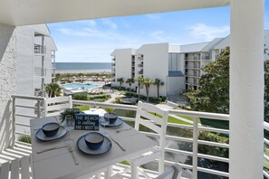 A balcony with a table set for dining, overlooking a pool and a beach.