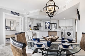 A modern kitchen with white cabinets, a central island, and a dining area with wicker chairs and blue tableware.