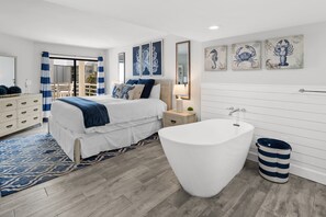 A modern bedroom with a large bed, a bathtub, and a view of the balcony. - Ocean Views at Villamare 1404 in Palmetto Dunes, Right on the Beach! (Hilton Head Island)