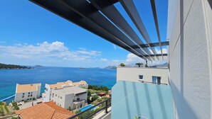 Un balcon avec vue sur la mer, des bâtiments aux toits couverts de tuiles et un ciel dégagé.