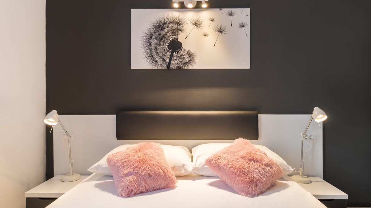 A bedroom with a bed, two bedside lamps, and a wall-mounted artwork.