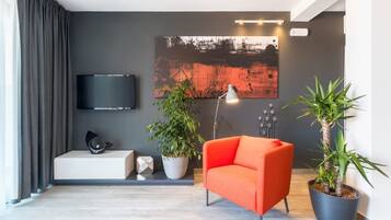 Una sala de estar moderna con un televisor de pantalla plana, un cuadro abstracto de gran tamaño, una planta en maceta, un sofá rojo y una lámpara de pie.