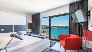 Une chambre d’hôtel moderne avec un grand lit, un fauteuil rouge, un bureau avec un ordinateur et une vue sur la mer.