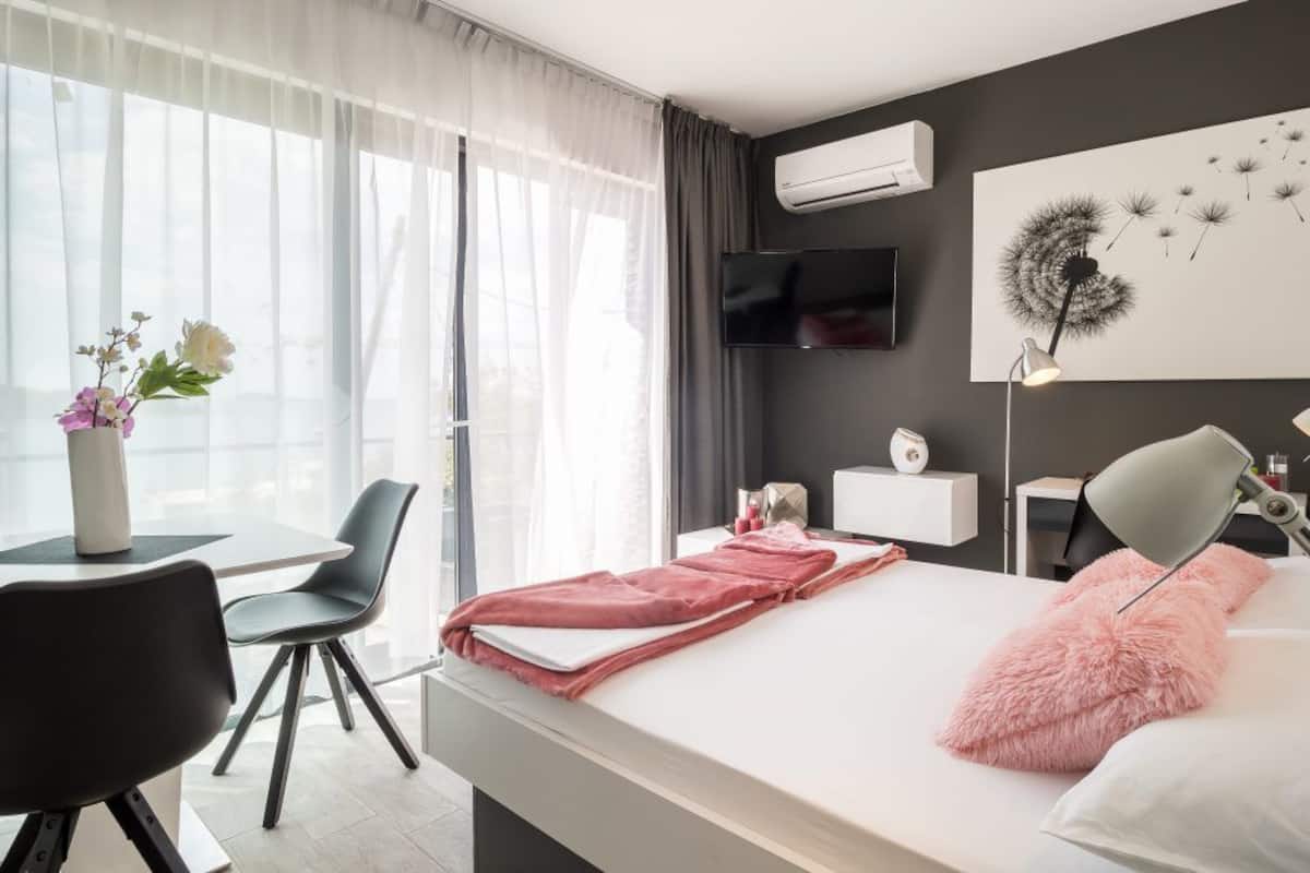Una habitación de hotel moderna con cama, mesita de noche, escritorio, sillas y un ventanal con cortinas.
