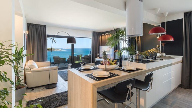 Une cuisine moderne avec un coin repas, de grandes fenêtres et une vue sur la mer.