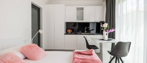A modern, compact living space with a kitchenette, a dining area, and a bed with pink accents.
