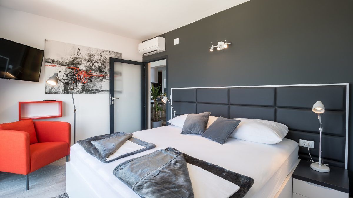 Une chambre moderne avec un grand lit, un fauteuil rouge, un téléviseur à écran plat et un tableau accroché au mur.