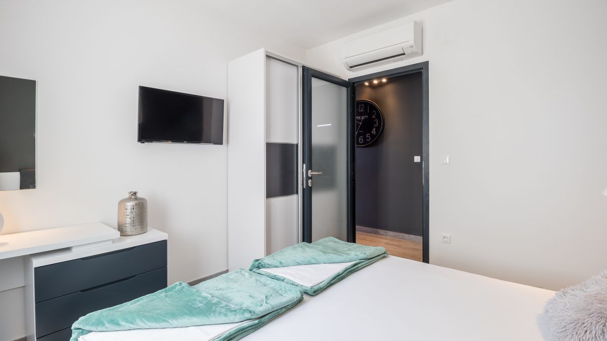 Un dormitorio con una cama, una mesita de noche, un televisor, un reloj y un armario.