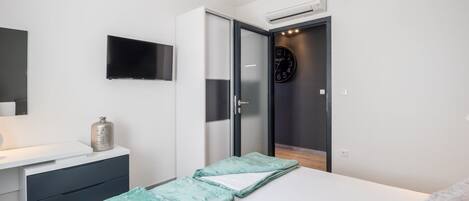 Un dormitorio con una cama, una mesita de noche, un televisor, un reloj y un armario.