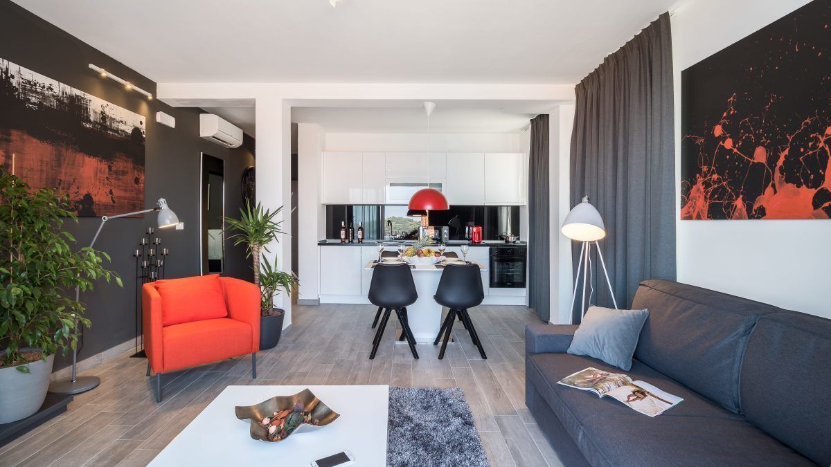 Una sala de estar moderna con un sofá gris, un sillón rojo y una zona de comedor con una mesa y sillas.
