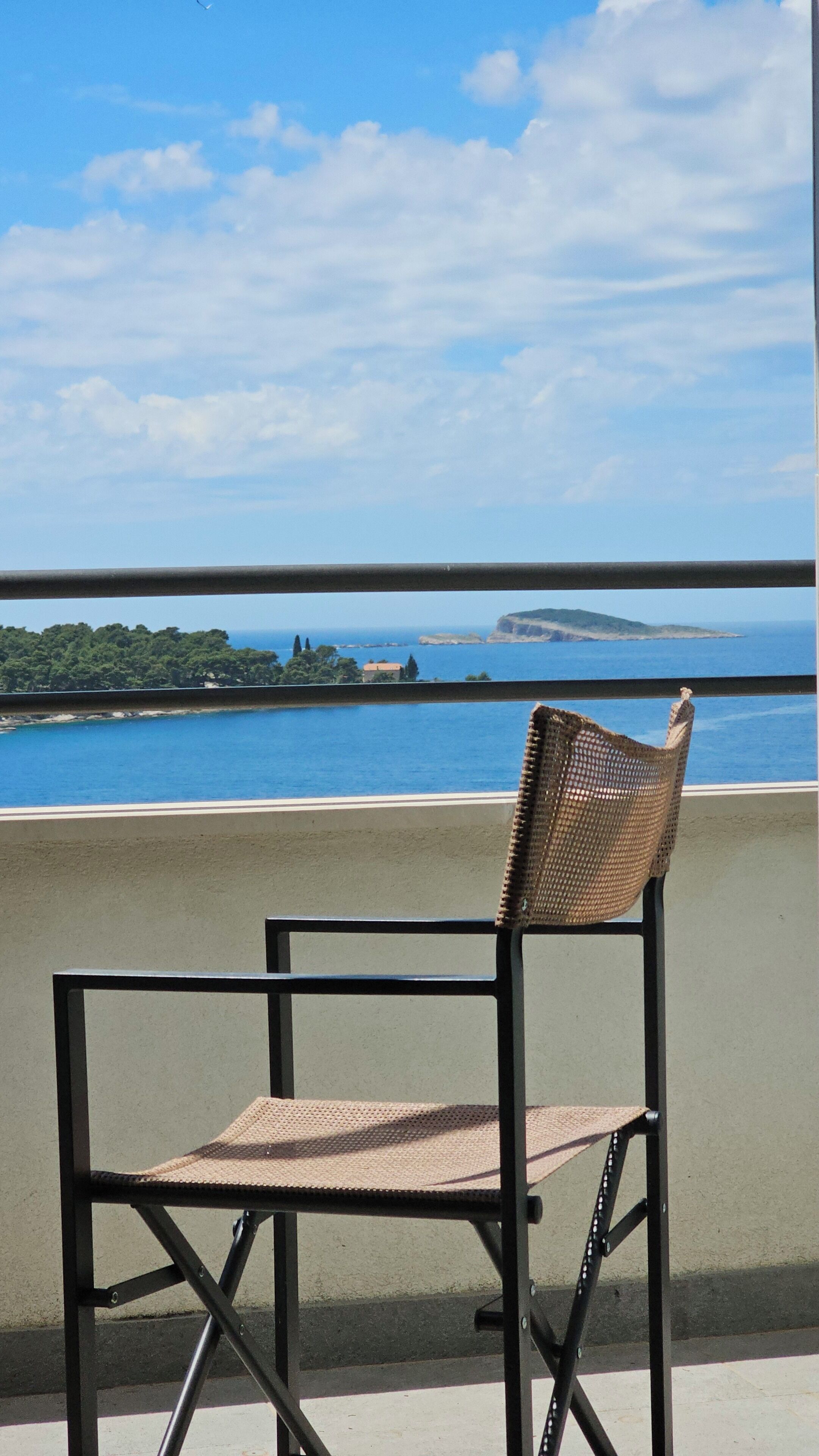 A chair on a balcony overlooking a coastal view with a clear sky and distant land.