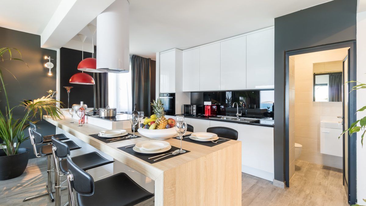 A modern kitchen with white cabinets, a central island with bar stools, and a red pendant light.