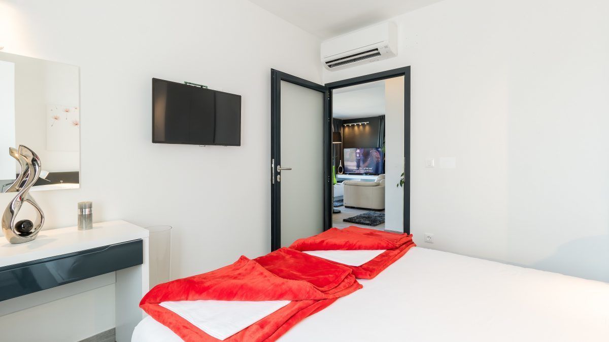 A modern hotel room with a bed, a bedside table, a mirror, and a TV.